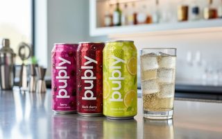 Chilled bubly POP cans and a clear highball glass with sparkling bubbles on a modern bar counter.