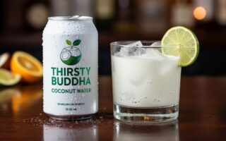 Chilled sparkling coconut water can next to a clear cocktail glass with ice, lime wedge, and visible rising bubbles.