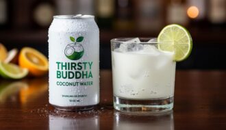 Chilled sparkling coconut water can next to a clear cocktail glass with ice, lime wedge, and visible rising bubbles.